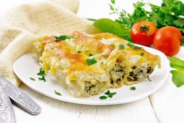 Süzme peynirle doldurulmuş Cannelloni ve tahta arka planda Bechamel soslu ıspanak, havlu, domates ve maydanoz.