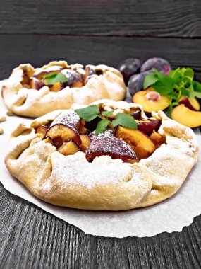 İki tatlı turta, erik, şeker ve parşömen üzerinde kakule, tahta bir arka planda nane filizi