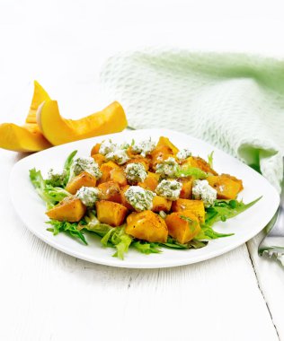 Fırında balkabağı salatası, tuzlu peynirli roka, ballı baharatlı hardal, sarımsak ve sebze yağı tabakta, peçete ve çatal ahşap arka planda.