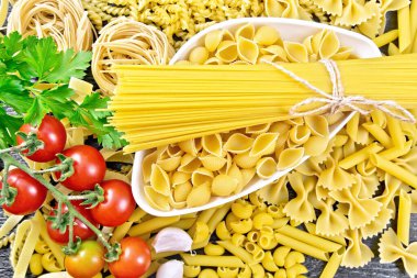 Kavanozda makarna, makarna ve spagetti, pipo rigate, tagliatelle, fusilli, penne, farfalle, fatih, trenette, rotini, pappardelle, domates, sarımsak ve maydanoz yukarıdan ahşap arka planda