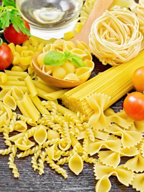 Kaşık içinde makarna kabukları, pipo rigonu, spagetti, tagliatelle, fusilli, penne, farfalle, trenette, rotini, domates, sarımsak, sebze yağı sürahide ve tahta zeminde maydanoz.