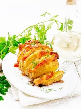 Fırında patates, tütsülenmiş pastırma ve peynirle kaplanmış, havlunun üstünde, ahşap bir arka planda.