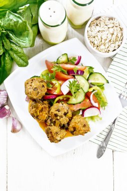 Ispanaklı kıymalı köfte, yulaf ezmesi ve domates soslu yeşil soğan, tabakta sebze salatası, yukarıdan ahşap bir arka planda havlu.