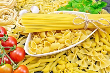 Kabın içinde makarna, makarna ve spagetti, pipo rigate, tagliatelle, fusilli, penne, farfalle, fatih, trenette, rotini, pappardelle, domates, ahşap zeminde sarımsak ve maydanoz.