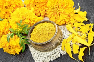 Çuval bezinde bir kasede İmeretian safranı, taç yaprakları ve siyah tahta arka planda Taze Tagetes çiçekleri