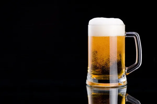 Mug fresh beer with cap of foam on a black background — Stock Photo, Image