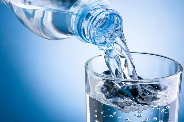 Verter agua de la botella en vidrio sobre fondo azul — Foto de Stock