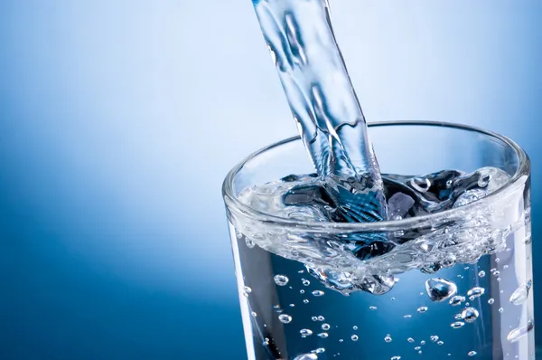 Verter agua en un vaso sobre fondo azul — Foto de Stock