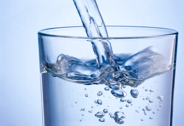 Primer plano vertiendo agua en un vaso sobre un fondo azul — Foto de Stock