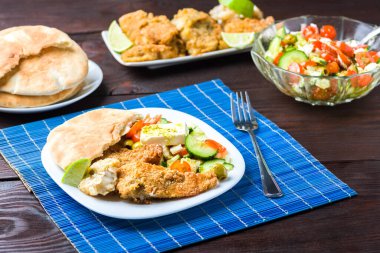 Fırında balık, sebze salatası, peynir ve pide ile servis edilir.