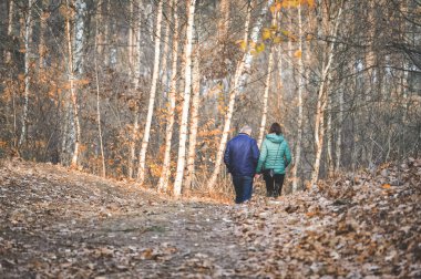 Ormanda sonbahar yürüyüşünde el ele tutuşan orta yaşlı bir çift.