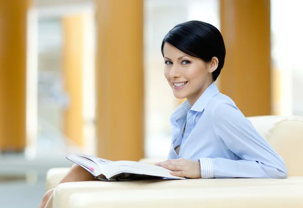 Pretty businesswoman rests at the sofa with book Stock Picture