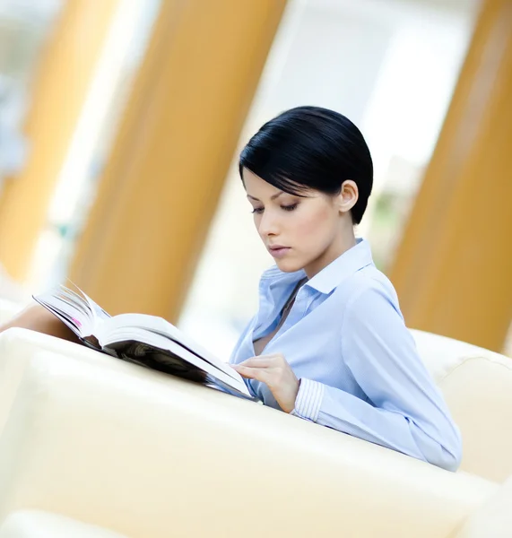 Mulher descansa no sofá com livro — Fotografia de Stock