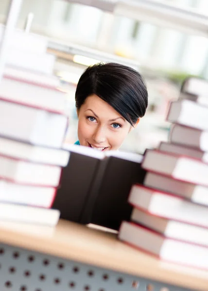 Estudante feminina está rodeada de pilhas de livros — Fotografia de Stock