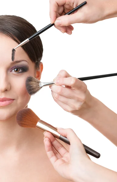 Three hands applying cosmetics on the woman's face Stock Picture