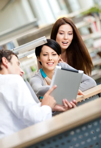 在图书馆的年轻男子和两个女人显示平板电脑 免版税图库图片