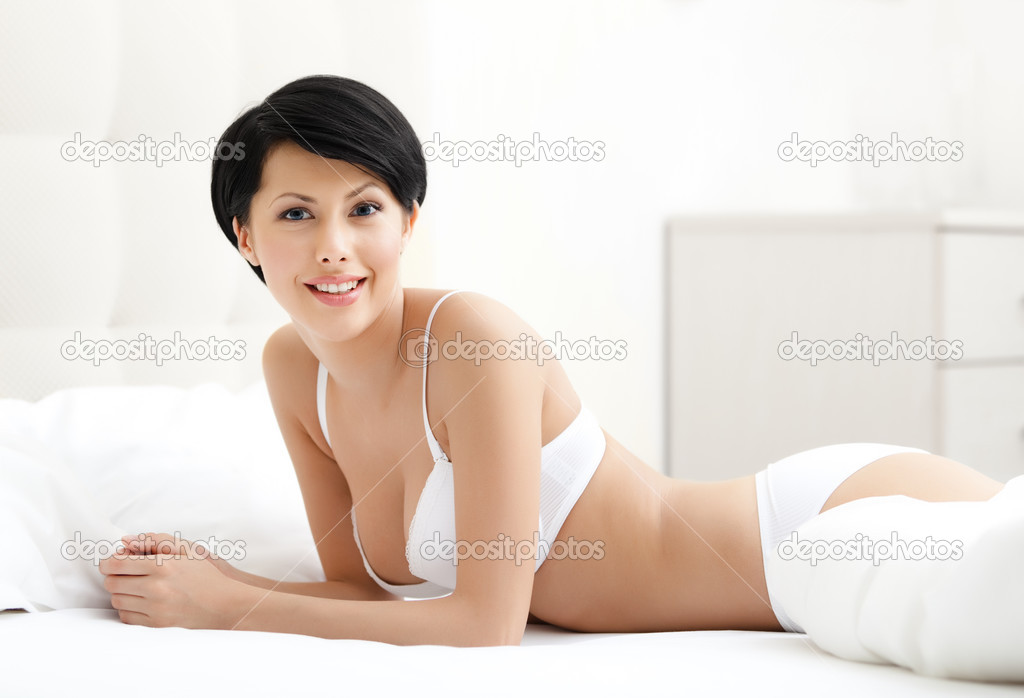 Woman in white bra is lying in the queensize bed