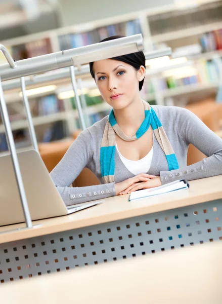 Étudiante travaillant sur l'ordinateur portable en argent assis au bureau de la bibliothèque — Photo