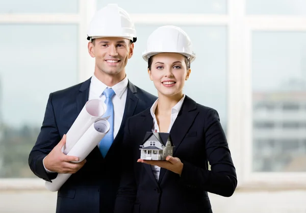 Dois empreiteiros mantendo plantas e casa modelo — Fotografia de Stock