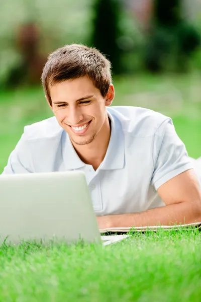 Mens liggend op het groene gras werken op de laptop — Stockfoto