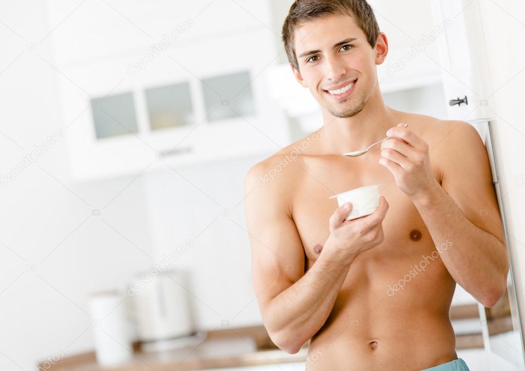 Half-naked young man eating yoghurt