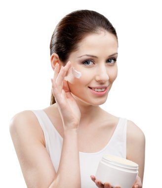 Woman putting on moisture cream from container on face clipart
