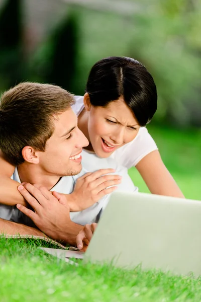 Paar liggend op het groene gras met zilveren laptop — Stockfoto