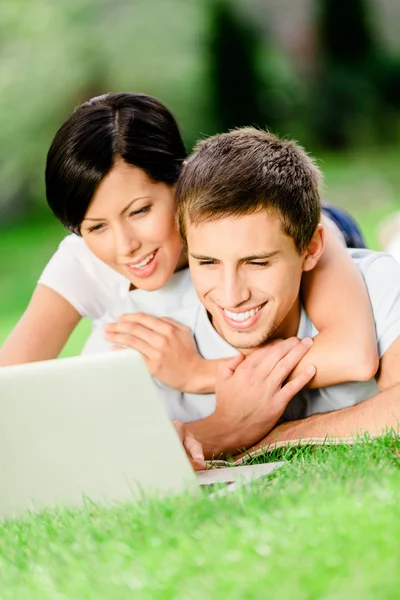 Paar liegt mit silbernem Computer im Gras — Stockfoto
