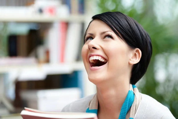 Estudiante riéndose con libro en la biblioteca — Foto de Stock