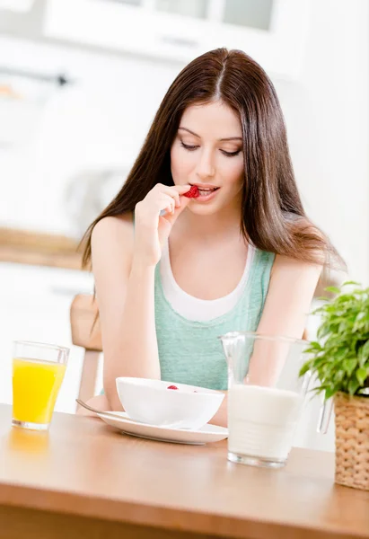 Retrato da menina comendo muesli dieta com leite e suco de morango e cítricos sentado na mesa da cozinha — Fotografia de Stock