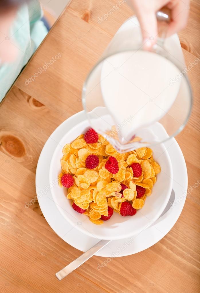 Top view of hand pouring milk into the plate with cereals and strawberry