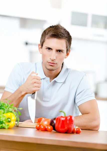 Hombre con cuchillo va a preparar el desayuno mientras está sentado en la mesa de la cocina llena de comida saludable — Foto de Stock