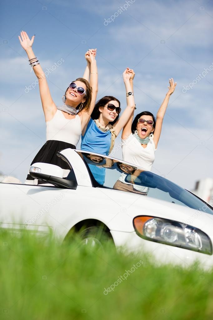 Friends stand in the white car with hands up