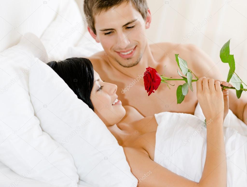 Man lying in bed gives scarlet rose to woman
