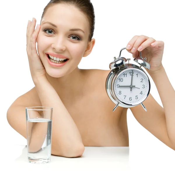 Naked girl with glass of water shows alarm clock — Stock Photo, Image