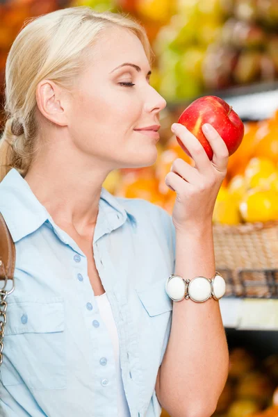 Girl at the shop choosing fruits smells apple — Stock Photo, Image