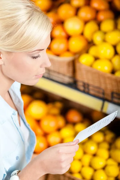 Tjejen ser genom inköpslista nära stacken av frukter — Stockfoto