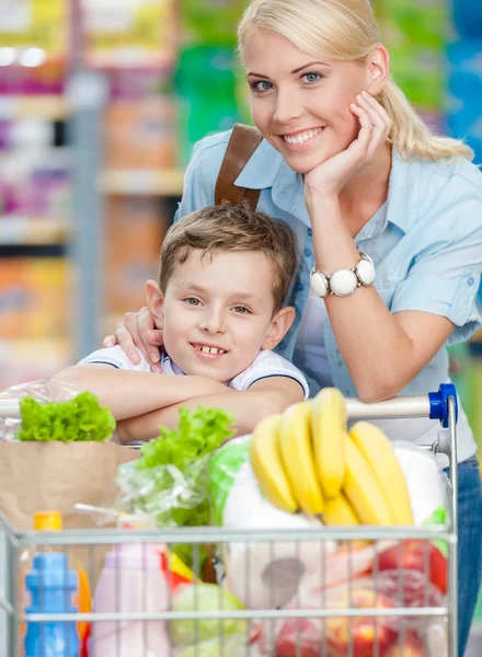 Mor och son med vagn full av produkter i köpcentrum — Stockfoto