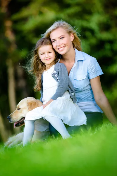 Madre e hija con labrador se sientan en la hierba — Foto de Stock