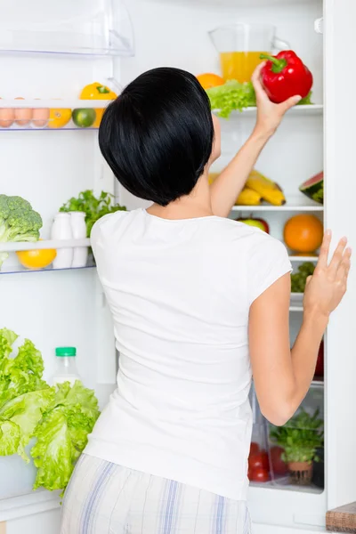 Mulher leva pimenta vermelha do refrigerador aberto — Fotografia de Stock