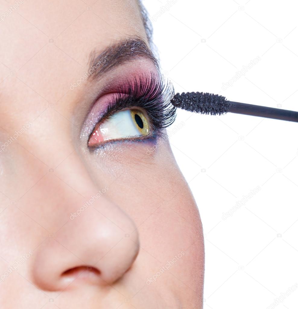Female eye with bright makeup and brush applying mascara on eyelashes