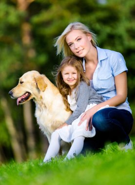 Yeşil çimenlerin üzerinde anne ve kızı ile golden retriever vardır