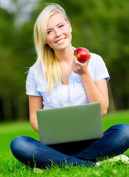 Ragazza con computer portatile e mela seduta sull'erba — Foto Stock