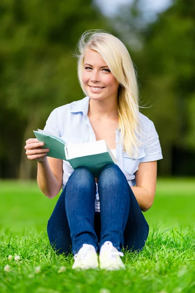 Frau liest Buch sitzt auf dem grünen Gras — Stockfoto