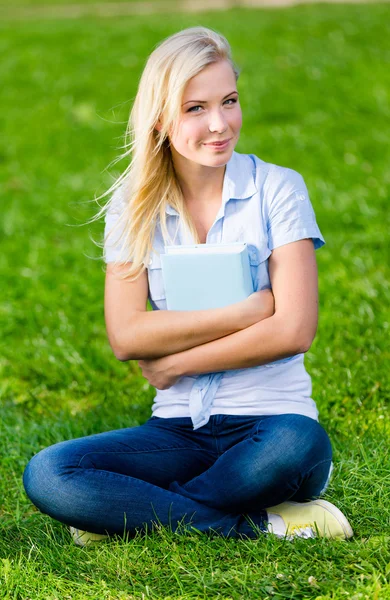 Estudante feminina segurando livro senta-se na grama — Fotografia de Stock