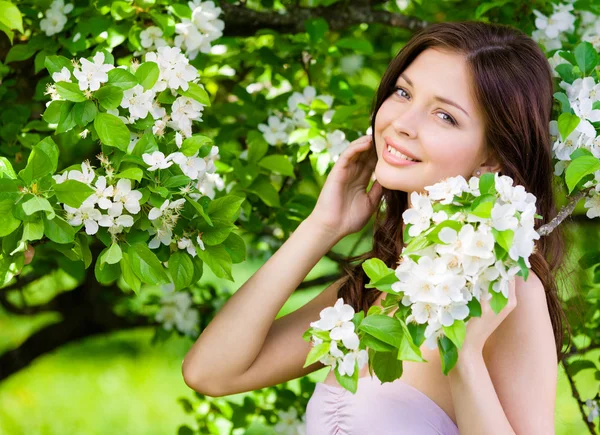 Beautiful woman touches face near the flowered tree — Stock Photo, Image