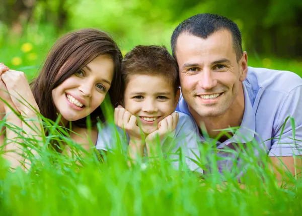 Familia feliz de tres tumbados en la hierba —  Fotos de Stock