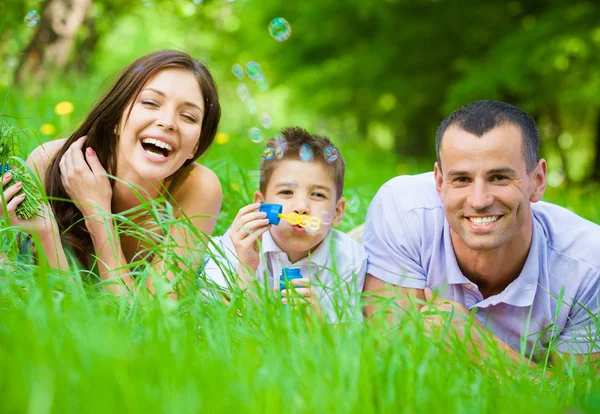 Familj på tre liggande på gräs och blåser bubblor — Stockfoto