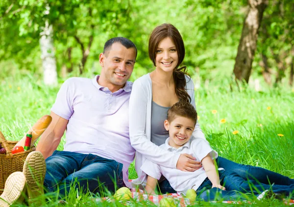 Happy family of three has picnic in green park — Stock Photo, Image