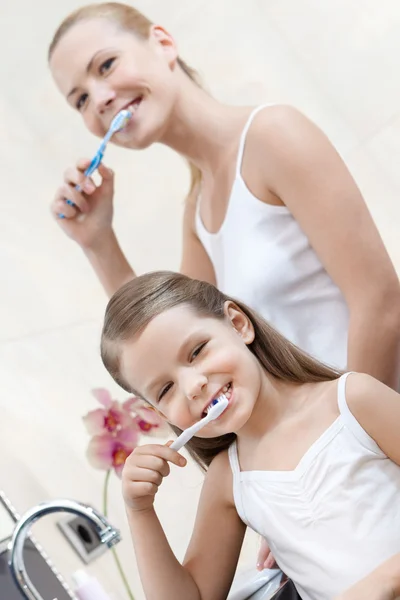Kislány tisztítja a fogakat anyukája — Stock Fotó